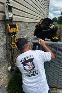 A technician in a white shirt works on an outdoor air conditioning unit.