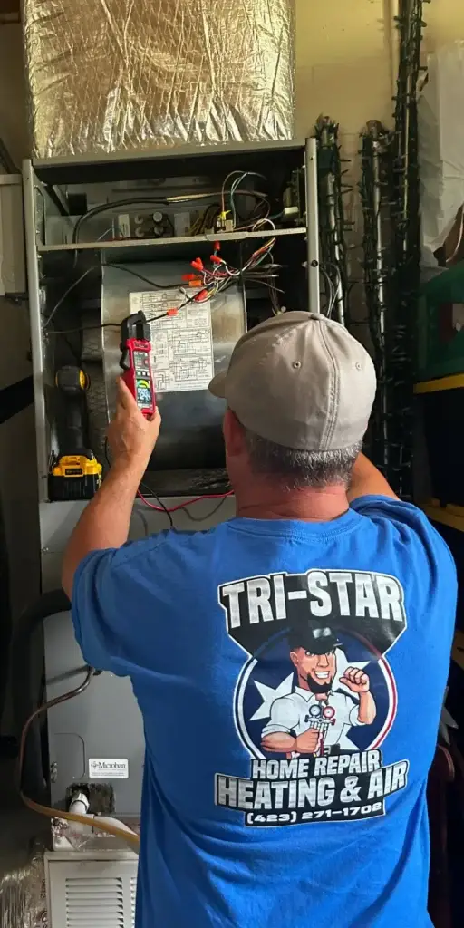 HVAC technician in Tri-Star logo shirt servicing a residential furnace unit.